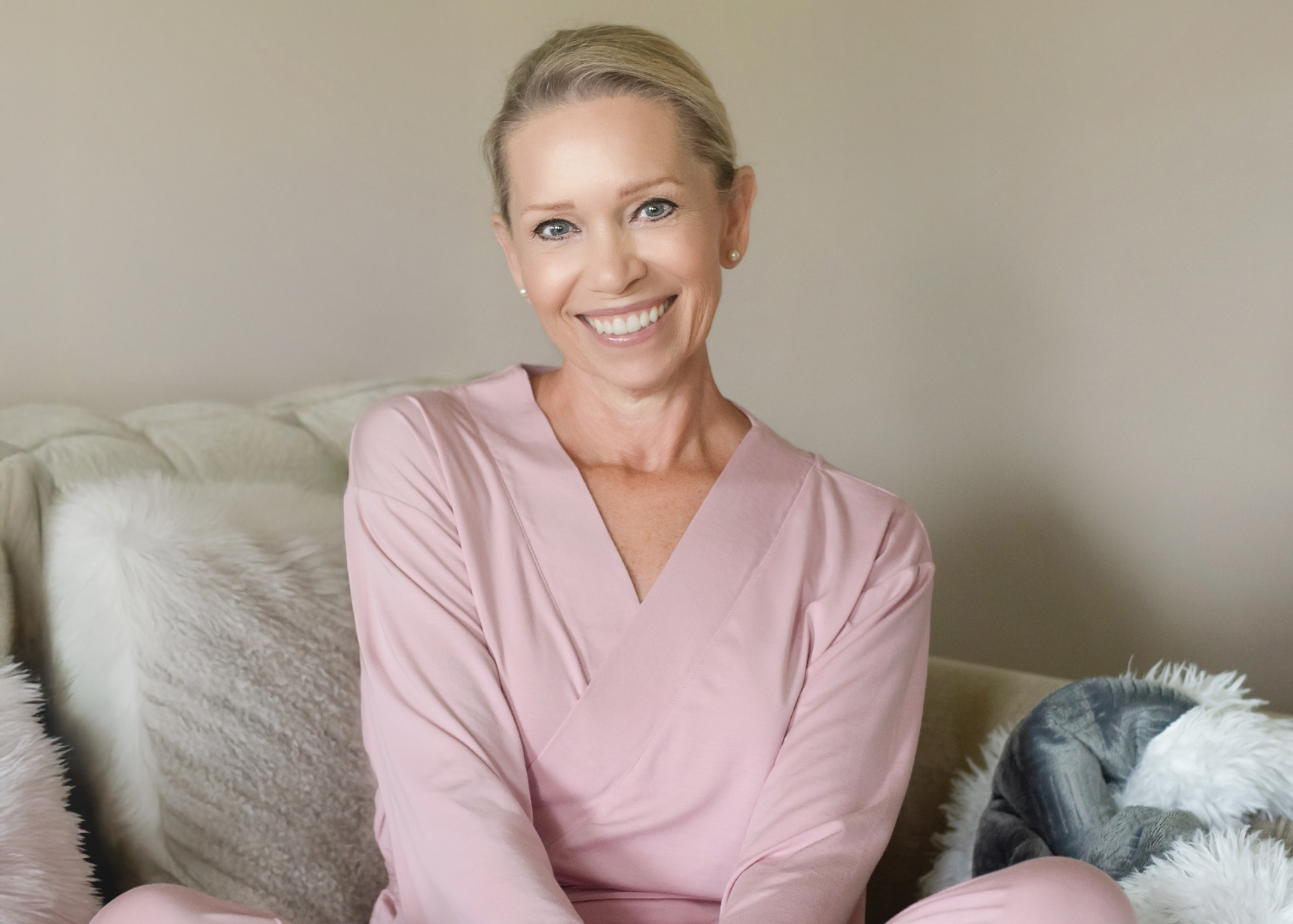 Woman wearing pink mastectomy pajamas sitting on a couch with a neutral background