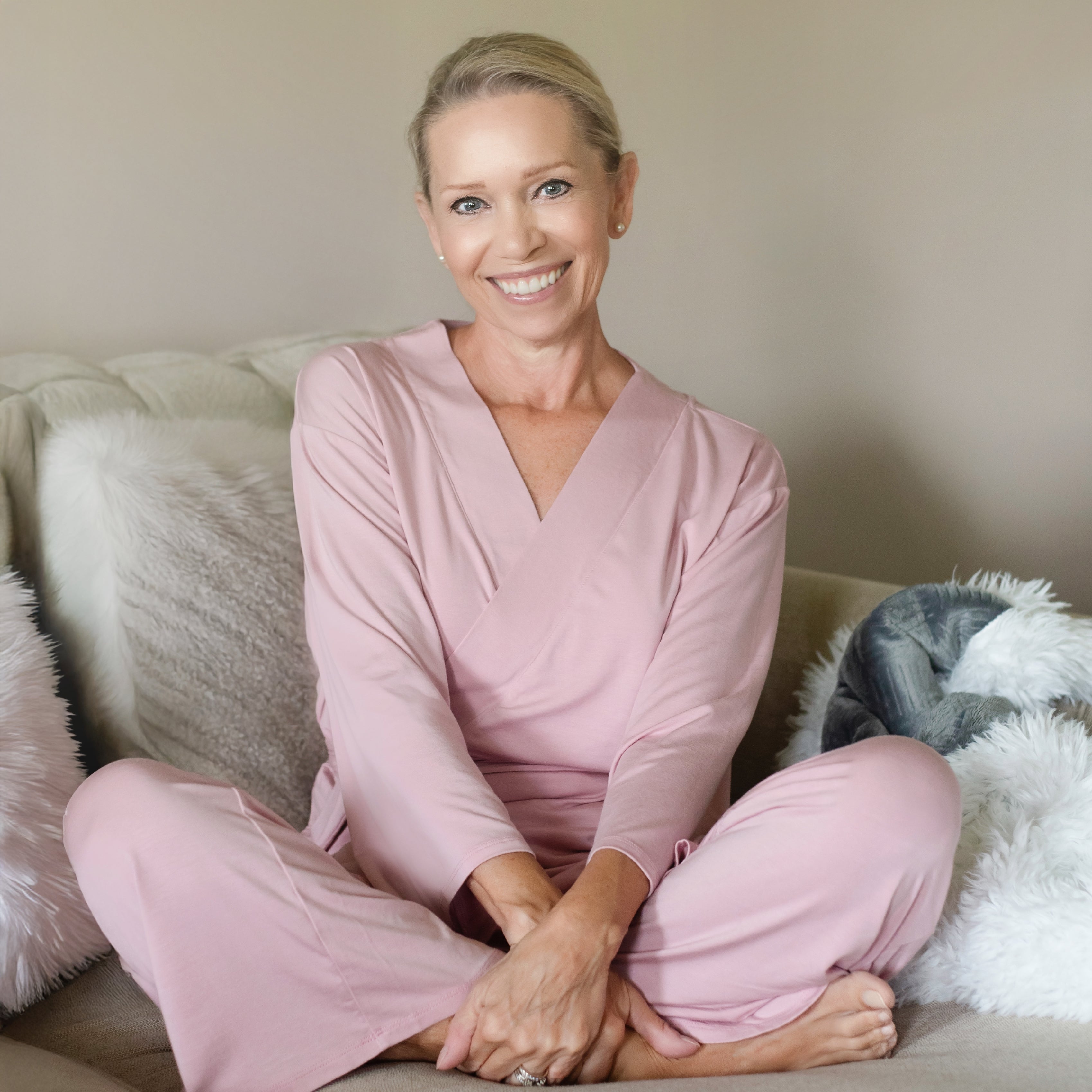 Woman in pink recovery pajamas sitting on a couch with a neutral background